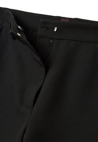 Pantaloni neri con una texture di tessuto liscia, caratterizzati da una cerniera metallica, chiusura con bottone e una vita sagomata. Include dettagli di cucitura sottili.