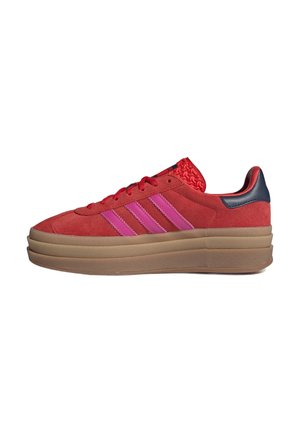 Red suede sneakers with pink stripes, a thick beige sole, and a patterned red accent on the back heel. Features round laces and a low cut.