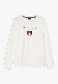 Witte sweatshirt met raglanmouwen, voorzien van een grijs geborduurd logo en een schild met rode en blauwe strepen. Zachte textuur, casual ontwerp.