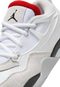 Zapatilla blanca con un revestimiento de ante gris texturizado, tela de malla, acentos rojos en el cuello y un logo negro en la lengüeta.