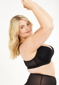 Musta rintaliivi, jossa on sileät kupit ja läpikuultavat verkkosivut. Suunnittelussa on säädettävät olkaimet ja saumatonta ilmettä.