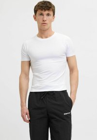 T-shirt blanc à manches courtes avec un col rond, associé à un pantalon noir à cordon de serrage avec des rayures sur les côtés et un accent de logo.