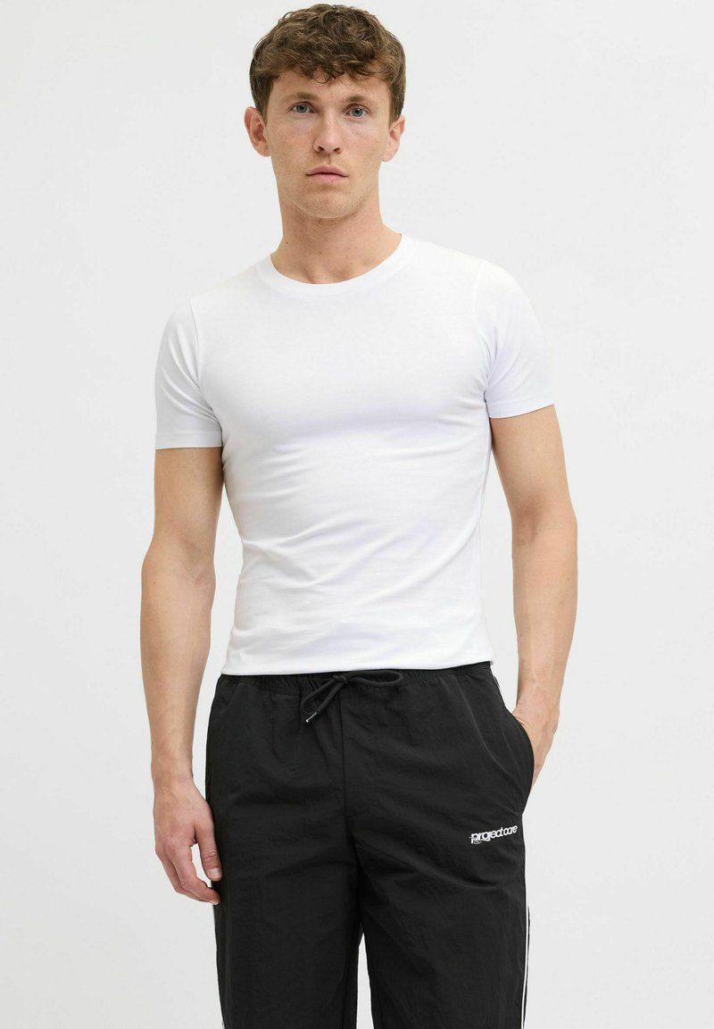 T-shirt blanc à manches courtes avec un col rond, associé à un pantalon noir à cordon de serrage avec des rayures sur les côtés et un accent de logo.