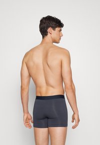 Boxer briefs cinzentos com um cós preto, apresentando um ajuste justo e uma textura suave. O modelo é visto de costas com um fundo neutro.