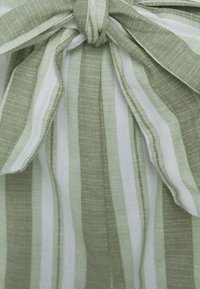 Tissu rayé avec des tons de vert et de blanc variés, doté d'une fermeture à nœud. Le matériau a une apparence texturée et tissée.