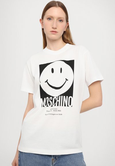Bílý bavlněný tričko s velkým černým smajlíkem a černým textem "Moschino." Krátké rukávy, design s kulatým výstřihem.