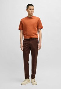 Kopparorange kortärmad ribbad skjorta med kontrasterande muddar, tillsammans med mörkbruna slim fit-byxor och ljusbeige sneakers.