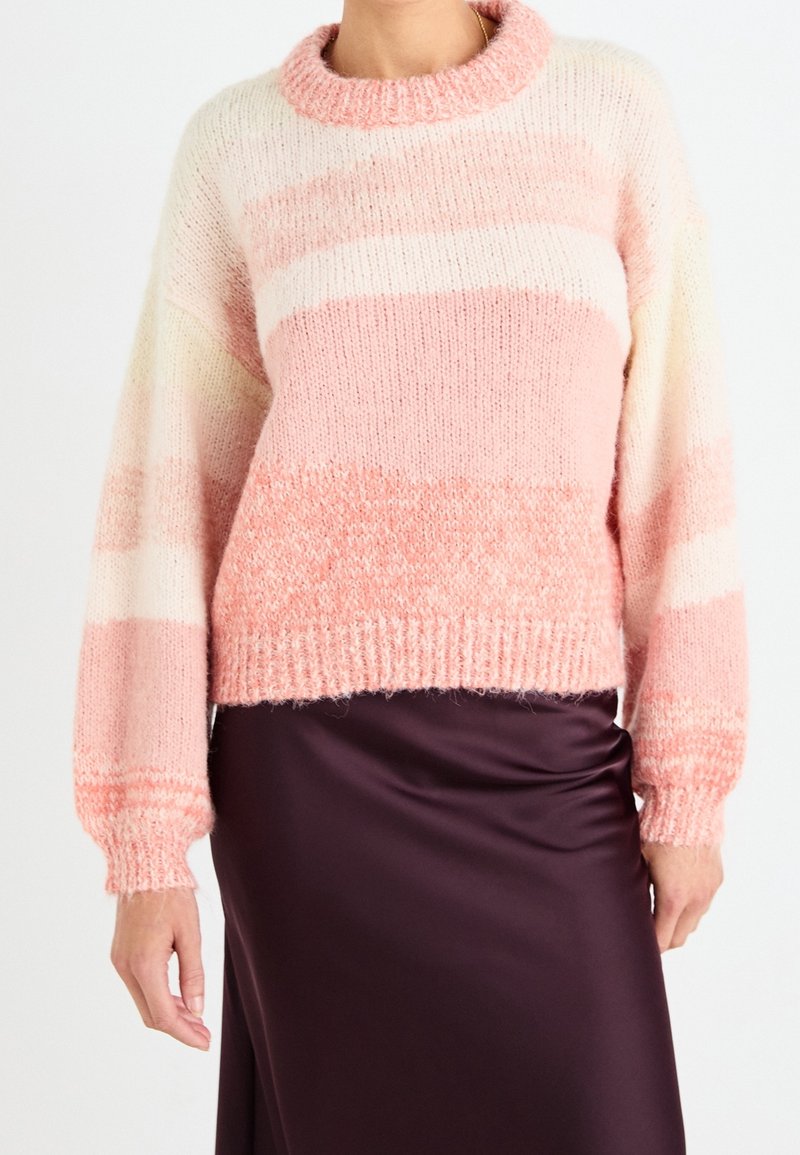 Femme portant un pull en maille rayé rose pâle et blanc avec des manches bouffantes, associé à une jupe en satin violet foncé.