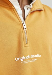 Felpa gialla con zip realizzata in tessuto misto cotone, con un alto colletto e logo testuale bianco "Originals Studio" sul davanti.