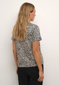 Camiseta de manga corta en blanco y negro con un patrón abstracto texturizado. Corte relajado con cuello redondo, hecha de una tela ligera.