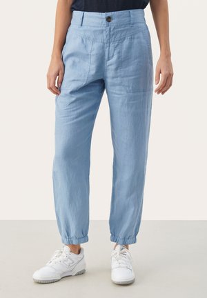 Pantalones casuales azul claro con bolsillos delanteros y puños elásticos, combinados con zapatillas blancas.