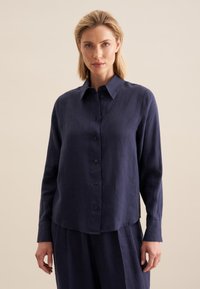 Chemise en lin bleu marine à manches longues, devant à boutons, et col pointu. Présente une texture subtile et une coupe décontractée, avec des boutons assortis au tissu.