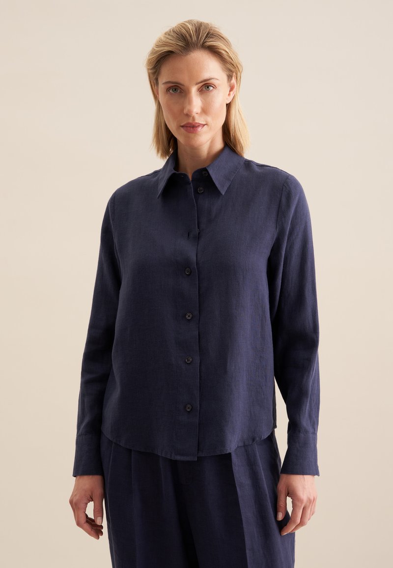 Chemise en lin bleu marine à manches longues, devant à boutons, et col pointu. Présente une texture subtile et une coupe décontractée, avec des boutons assortis au tissu.