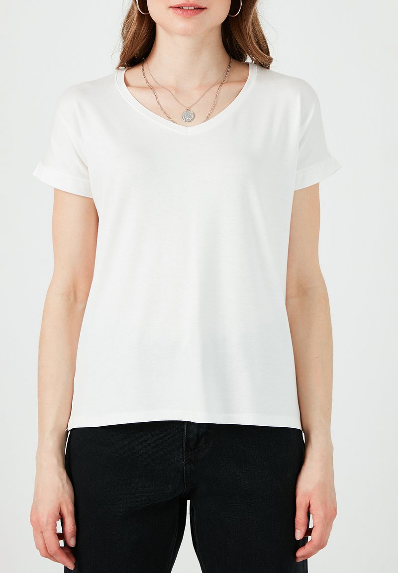 Hvid v-hals t-shirt med opsmøg ved korte ærmer, lavet af blødt stof. Har en lige pasform og bæres med sorte bukser.