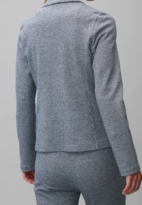 Texturovaný modrý kabát s houndstooth vzorem, s dlouhými rukávy, límcem a přiléhavým střihem, s čistým zakončením a jemnými detaily šití.