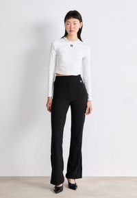 White long-sleeve crop top with "HUGO" logo, paired with black flared pants, and black pointed-toe shoes with embellishments. Smooth fabric textures.