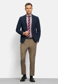 Navy blazer over a light purple shirt and striped tie, paired with beige trousers and black shoes. Flat front with button details.