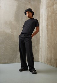 Black t-shirt with a small logo, relaxed-fit black trousers with side stripes, and black clogs. Smooth texture, minimalistic design.