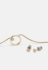 Collana d'oro con un pendente circolare che presenta una gemma trasparente, insieme a due paia di orecchini a perno con design a forma di cuore e rotondi.