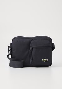 Borsa a spalla in tessuto nero con un ampio scomparto principale con zip, piccolo taschino frontale con zip, tracolla regolabile e logo ricamato di un coccodrillo.