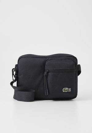 Borsa a spalla in tessuto nero con un ampio scomparto principale con zip, piccolo taschino frontale con zip, tracolla regolabile e logo ricamato di un coccodrillo.