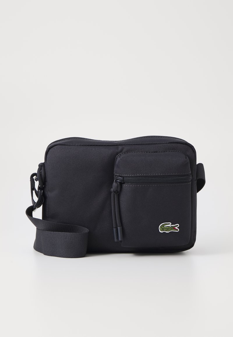 Borsa a spalla in tessuto nero con un ampio scomparto principale con zip, piccolo taschino frontale con zip, tracolla regolabile e logo ricamato di un coccodrillo.
