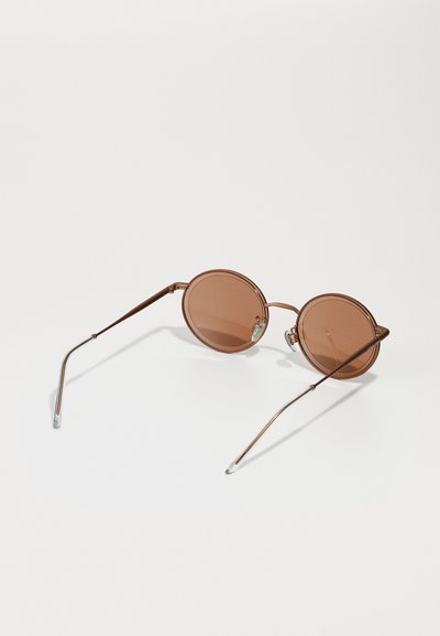 Round sunglasses with brown tinted lenses, thin metal frame, and slender arms. Features small nose pads and silver accents on the frame.