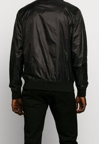 Czarna nylonowa kurtka bomber z prążkowanymi mankietami i pasem, charakteryzująca się gładką teksturą oraz elastycznymi ściągaczami dla dopasowania.