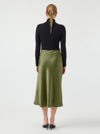 Een zwart top met lange mouwen gecombineerd met een mid-length olijfgroene satijnen rok. De outfit heeft een slim fit en vloeiende stof met een gladde textuur.