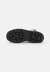 Talpă din cauciuc negru cu un model de uzură robust. Părți vizibile din partea superioară de nuanță deschisă, cu accente decorative și detalii de cusătură.