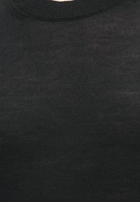 Κοντινή λήψη μαύρου ριμπ πλεκτού υφάσματος στον λαιμόκοψη και το επάνω μέρος του στήθους ενός ενδύματος.