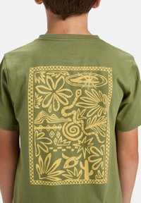 Green cotton t-shirt with a yellow graphic print featuring stylized plants, a snake, and geometric shapes on the back.