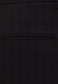 Mustat housut, joissa on taka-tasku kapealla aukolla, valmistettu sileästä, teksturoidusta kankaasta, jossa on hienovarainen kiilto ja siistit linjat.