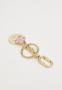 Llave de oro con un charm de flor rosa, un disco circular con el texto "Fiorala" y un resistente clasp de mosquetón.