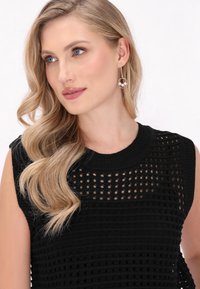 Maglione nero in maglia con un motivo testurizzato, caratterizzato da maniche corte e scollo rotondo, abbinato a orecchini a cerchio dorati e perle.