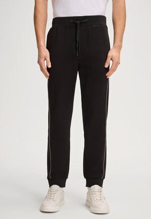 Zwarte sweatpants met een elastische enkelband, trekkoord in de taille en witte zijstrepen. Gemaakt van een zachte stof, ontworpen voor comfort.