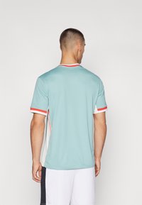 Camiseta deportiva de color azul claro con mangas cortas, paneles laterales blancos y acentos rojos en el cuello y los puños de las mangas.