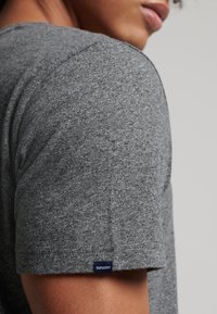 T-shirt grigio a maniche corte realizzato in tessuto testurizzato, con un piccolo etichetta blu "Superdry" sull'orlo e una silhouette aderente.
