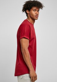 Tricou scurt, cu mânecă scurtă, de culoare vișinie, cu tivuri rulate, având un guler rotund și o croială lejeră. Confecționat dintr-un material moale din bumbac, cu un design minimal.