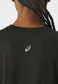 Zwart atletisch shirt met korte mouwen, voorzien van een ronde halslijn en een reflecterend logo op de rug. Gladde stoftextuur.