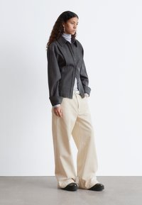 Gray button-up shirt with a structured fit, layered over a light gray turtleneck, paired with wide beige trousers and black platform shoes.