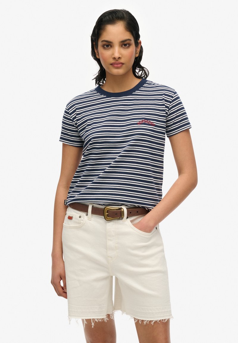 Camiseta de algodón a rayas en azul marino y blanco con mangas cortas y cuello redondo, combinada con pantalones cortos de denim blancos con bordes deshilachados.