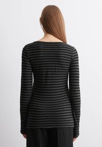 Langermet topp i svart med horisontale grå striper, med båtutringning og en tettsittende silhuett. Mykt, lett materiale.