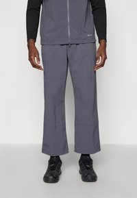 Gray, lightweight, moisture-wicking pants with a relaxed fit, featuring stitched panel details and worn with black athletic shoes.