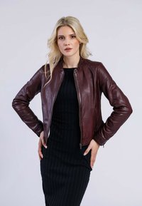 Veste en cuir bordeaux de style bombardier avec une fermeture éclair, design ajusté et col côtelé ; portée sur une robe noire côtelée. Texture lisse.