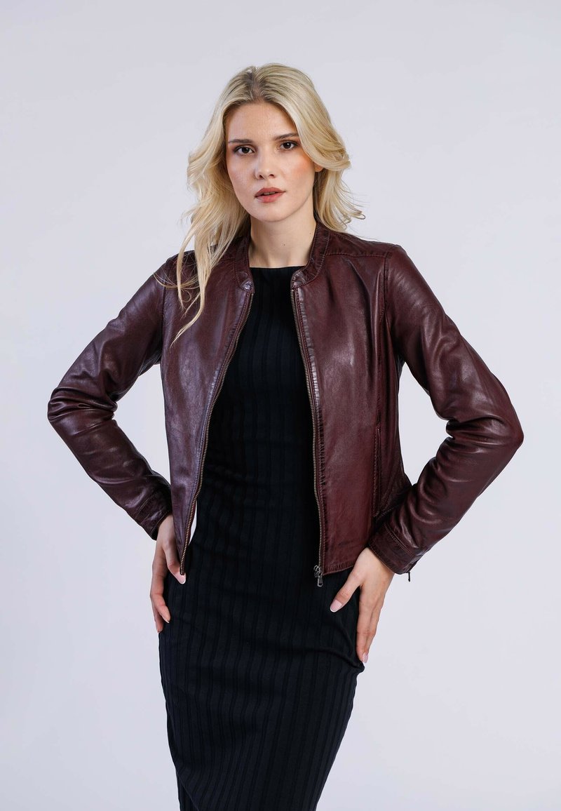 Veste en cuir bordeaux de style bombardier avec une fermeture éclair, design ajusté et col côtelé ; portée sur une robe noire côtelée. Texture lisse.