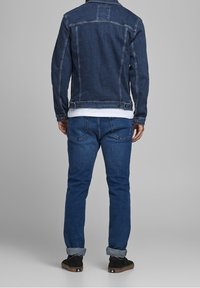 Men's dark blue denim jacket with a fitted design, featuring a classic collar and button closures. Paired with matching jeans, visible stitching details.