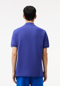 Lila pikétröja med korta ärmar och ribbad krage, med en slät textur och en jämn färg över hela.