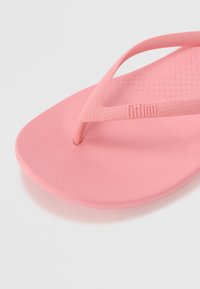 Roza natikača z teksturirano gumijasto podplato in thong trakom, ki ima logo na traku. Gladek zaključek z obliko, ki se prilega.