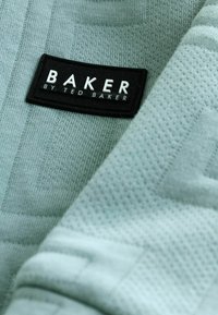 Himmelblauer Stoff mit einem strukturierten Muster; verfügt über ein schwarzes Etikett mit der Aufschrift "BAKER by TED BAKER", das die Marke hervorhebt.